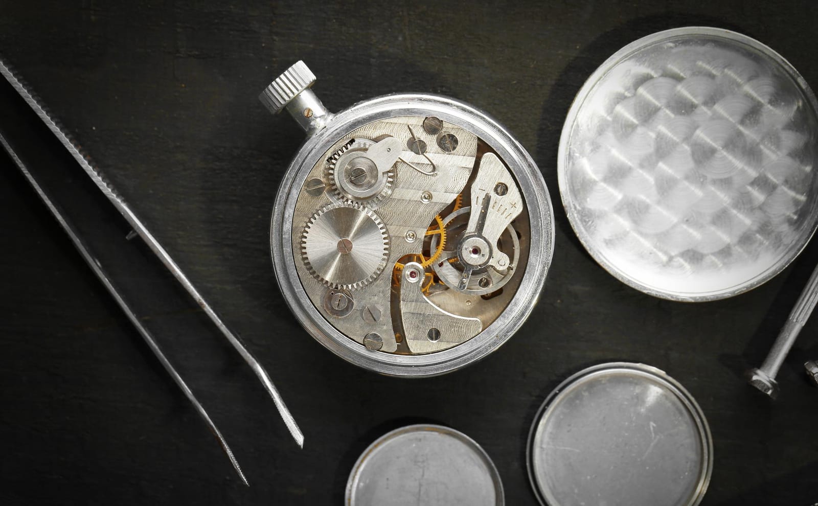Mani di un orologiaio che assemblano con pinzette un movimento d'epoca